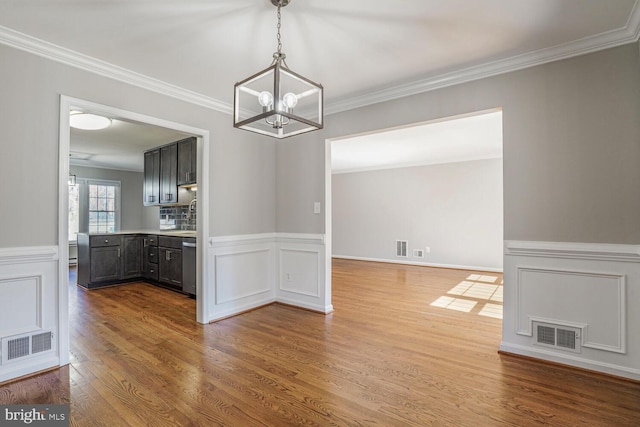 unfurnished dining area featuring visible vents, wood finished floors, wainscoting, and ornamental molding