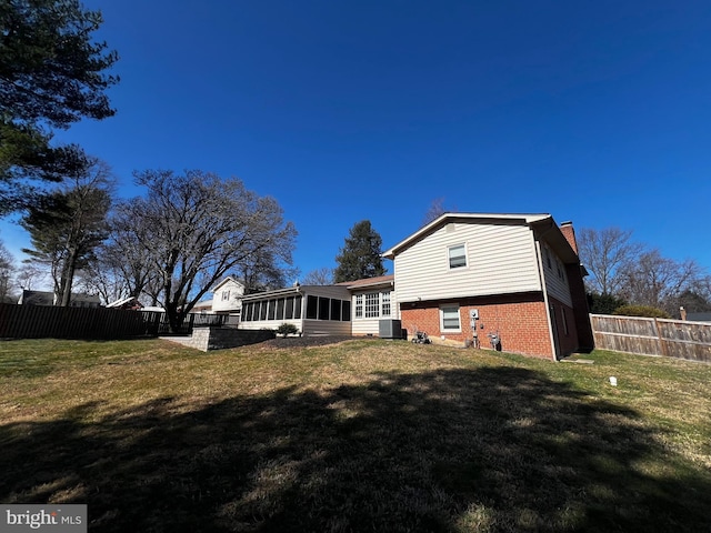 rear view of property featuring fence, a yard, a sunroom, brick siding, and a chimney