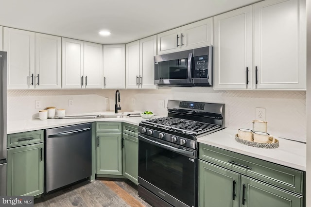 kitchen with wood finished floors, stainless steel appliances, green cabinets, white cabinets, and light countertops