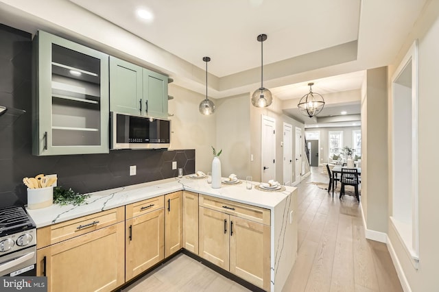 kitchen featuring light wood finished floors, backsplash, light brown cabinetry, a peninsula, and stainless steel appliances