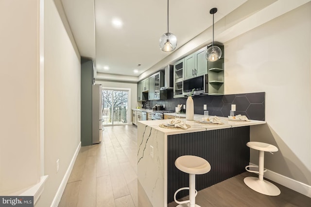 kitchen with backsplash, green cabinets, wall chimney range hood, stainless steel appliances, and open shelves