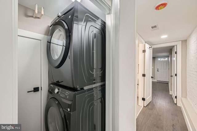 washroom with stacked washer / drying machine, visible vents, wood finished floors, and laundry area