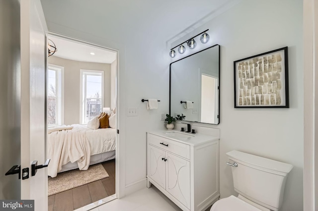 bathroom with toilet, wood finished floors, connected bathroom, baseboards, and vanity