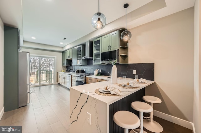 kitchen featuring a peninsula, stainless steel appliances, green cabinets, wall chimney exhaust hood, and backsplash