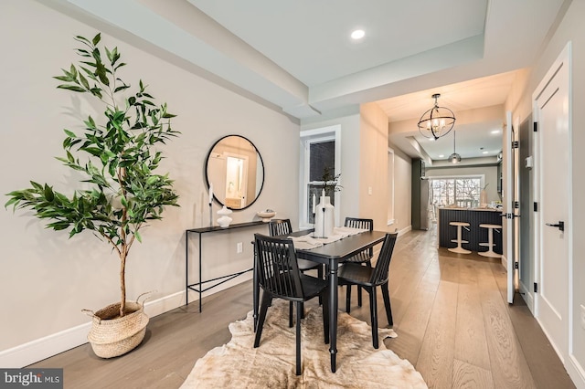 dining area with a notable chandelier, a raised ceiling, baseboards, and wood finished floors