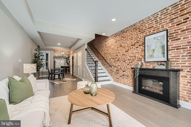 living room featuring a glass covered fireplace, wood finished floors, brick wall, baseboards, and stairs