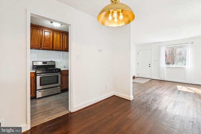 kitchen featuring baseboards, gas range, backsplash, and dark wood finished floors