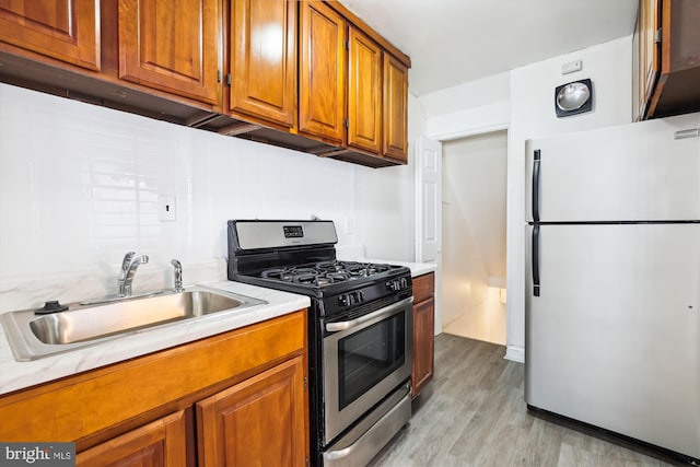 kitchen with brown cabinets, a sink, freestanding refrigerator, light countertops, and gas range