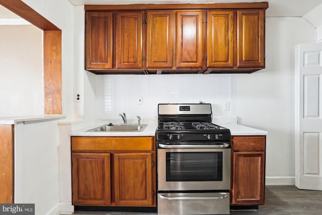 kitchen featuring brown cabinetry, light countertops, stainless steel range with gas cooktop, and a sink