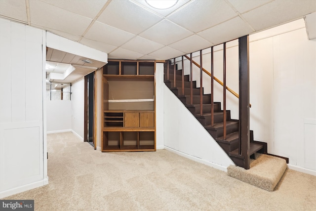 finished below grade area with stairs, a drop ceiling, baseboards, and carpet floors