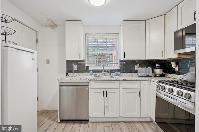 kitchen with light stone countertops, decorative backsplash, stainless steel appliances, light wood-style floors, and white cabinetry