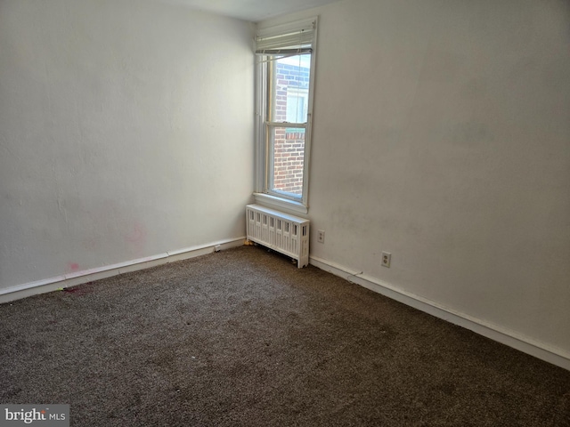 spare room featuring radiator and dark colored carpet