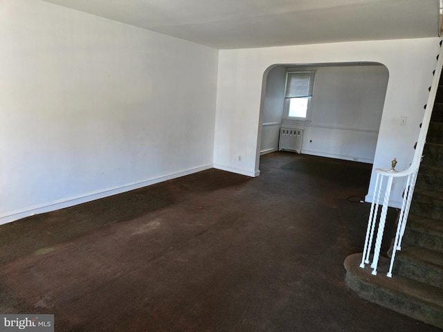 unfurnished room featuring baseboards, stairway, concrete flooring, radiator heating unit, and arched walkways