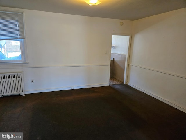 unfurnished room with radiator and dark colored carpet