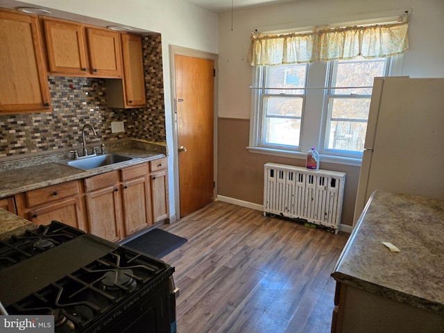 kitchen with black gas stove, radiator heating unit, freestanding refrigerator, a sink, and light wood-type flooring