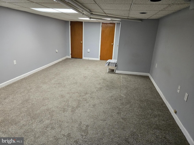 finished below grade area featuring carpet flooring, a paneled ceiling, and baseboards