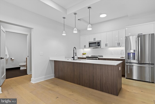 kitchen featuring light wood-type flooring, a sink, backsplash, stainless steel appliances, and a peninsula