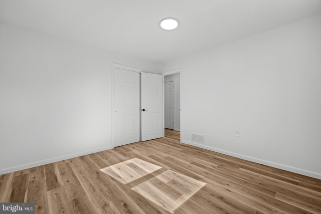 unfurnished bedroom with light wood finished floors, visible vents, a closet, and baseboards