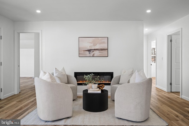 living area featuring a glass covered fireplace, recessed lighting, wood finished floors, and baseboards