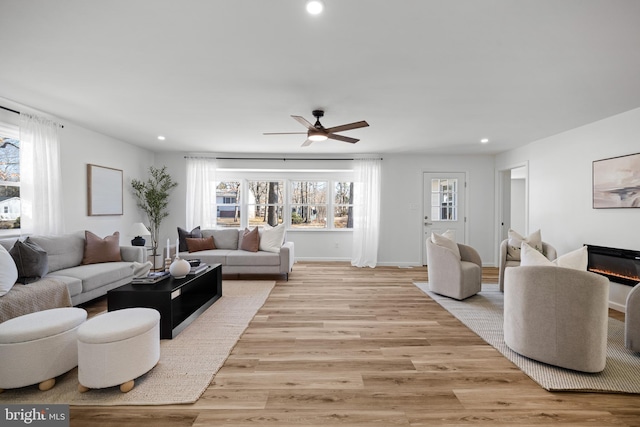 living area with a glass covered fireplace, recessed lighting, light wood-style floors, and baseboards