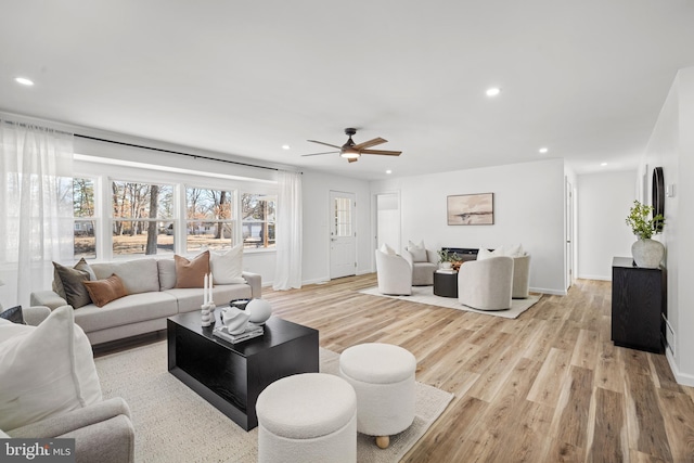 living room featuring a ceiling fan, baseboards, recessed lighting, a warm lit fireplace, and light wood-type flooring