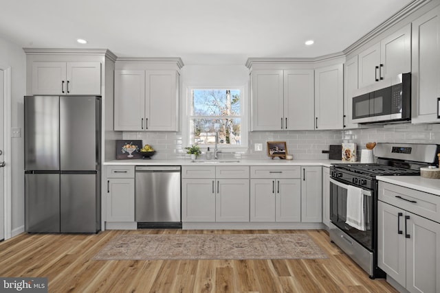 kitchen featuring a sink, stainless steel appliances, light wood-style floors, light countertops, and decorative backsplash