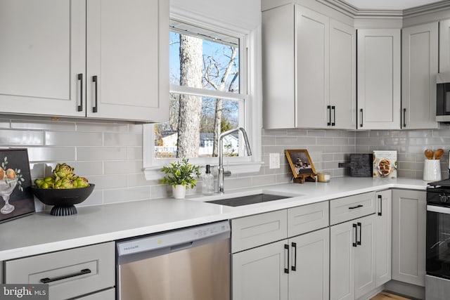 kitchen featuring gray cabinets, stainless steel appliances, light countertops, and a sink