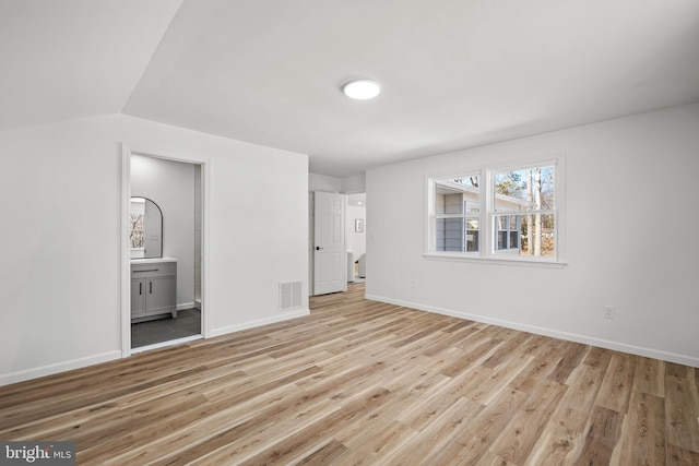 unfurnished bedroom with light wood-type flooring, visible vents, connected bathroom, baseboards, and vaulted ceiling