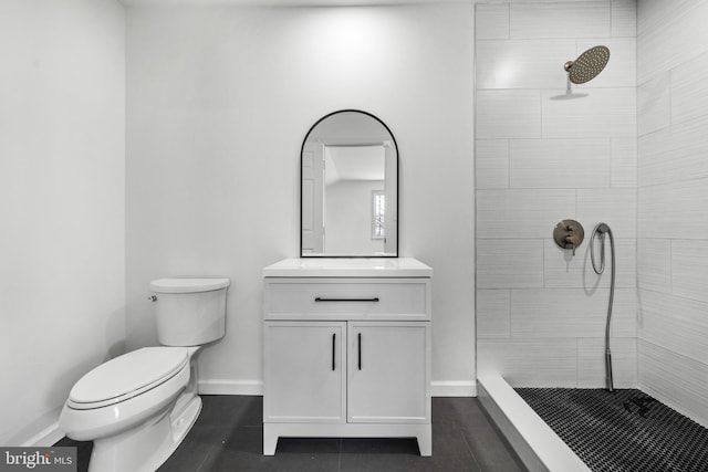 bathroom featuring a tile shower, toilet, vanity, and baseboards