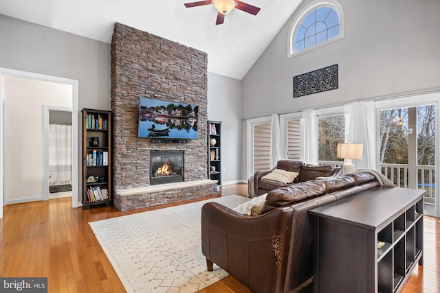 living room featuring a stone fireplace, high vaulted ceiling, light wood-type flooring, and ceiling fan