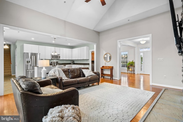 living area with a ceiling fan, stairway, light wood-style floors, and baseboards