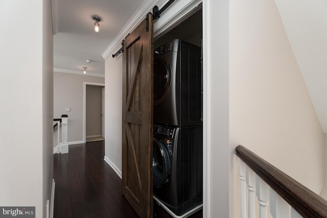 washroom with laundry area, dark wood-style flooring, ornamental molding, stacked washer and dryer, and a barn door