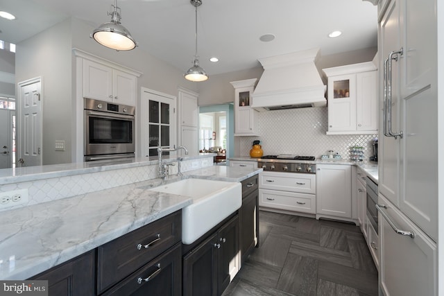 kitchen with premium range hood, white cabinetry, appliances with stainless steel finishes, and a sink