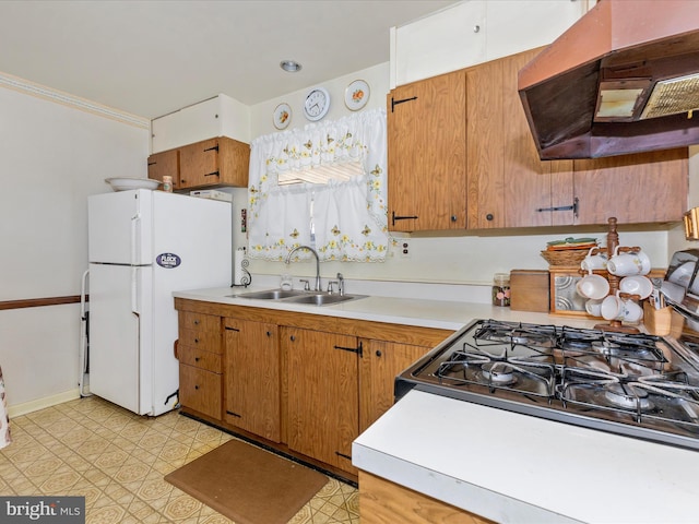 kitchen featuring light countertops, exhaust hood, freestanding refrigerator, and a sink