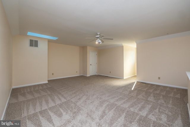 empty room featuring visible vents, baseboards, carpet flooring, a skylight, and a ceiling fan