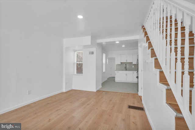 unfurnished living room with stairway, visible vents, recessed lighting, a sink, and light wood-style floors