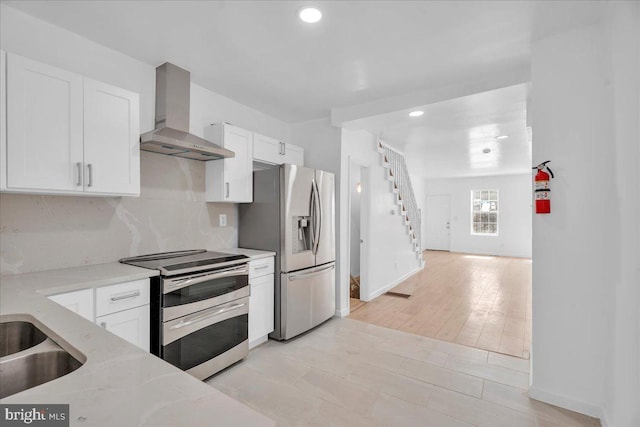 kitchen with light stone counters, a sink, white cabinets, appliances with stainless steel finishes, and wall chimney exhaust hood