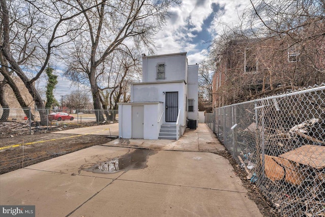 rear view of house with stucco siding, fence, central AC unit, and entry steps