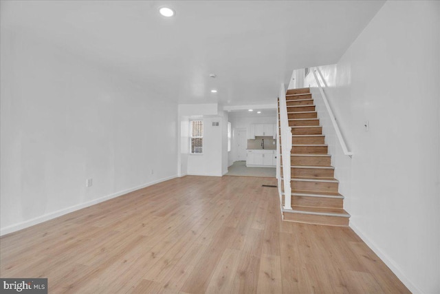 unfurnished living room with stairway, baseboards, recessed lighting, a sink, and light wood-style floors