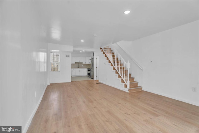 unfurnished living room with recessed lighting, light wood-type flooring, baseboards, and stairs