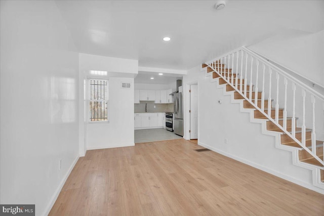 unfurnished living room with stairway, light wood-style flooring, baseboards, and visible vents