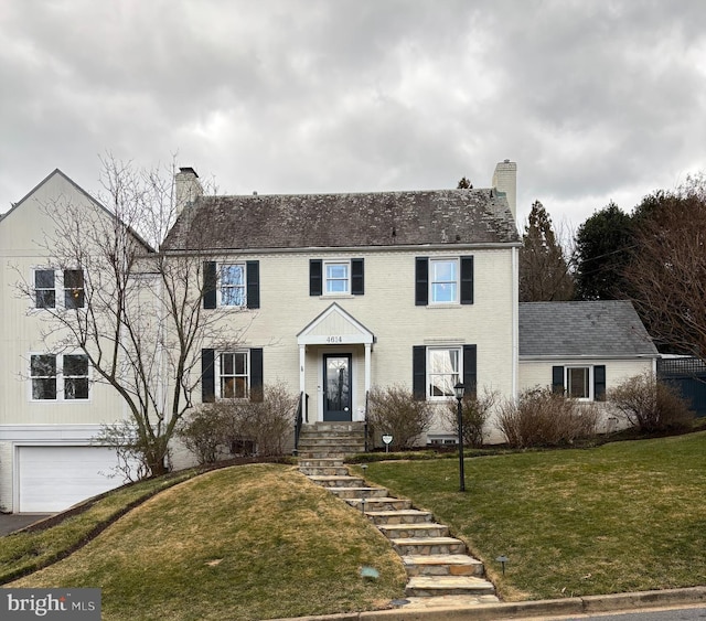 colonial-style house with a garage, a front lawn, and a chimney