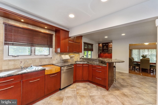 kitchen with a healthy amount of sunlight, a peninsula, a sink, decorative backsplash, and stainless steel dishwasher