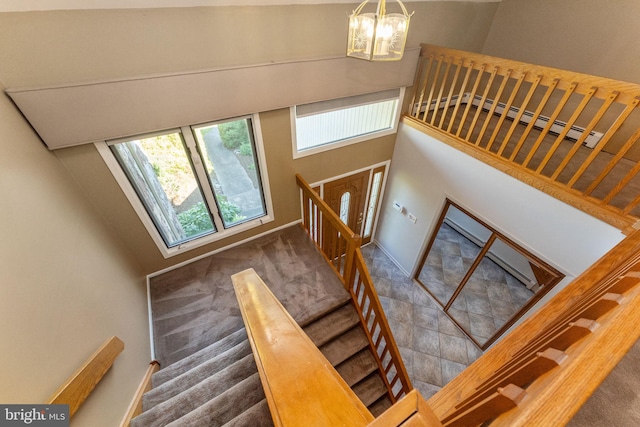 staircase featuring a notable chandelier, baseboards, a towering ceiling, and carpet floors