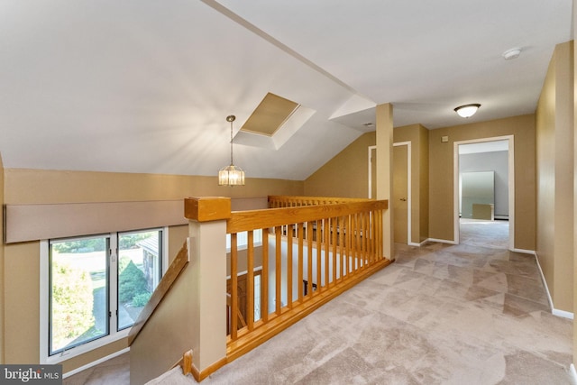 hallway featuring an upstairs landing, a notable chandelier, vaulted ceiling with skylight, carpet flooring, and baseboards