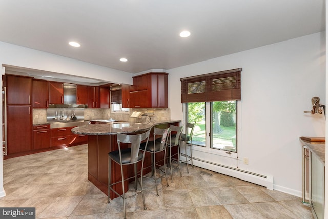 kitchen with decorative backsplash, a breakfast bar area, wall chimney exhaust hood, and a baseboard radiator