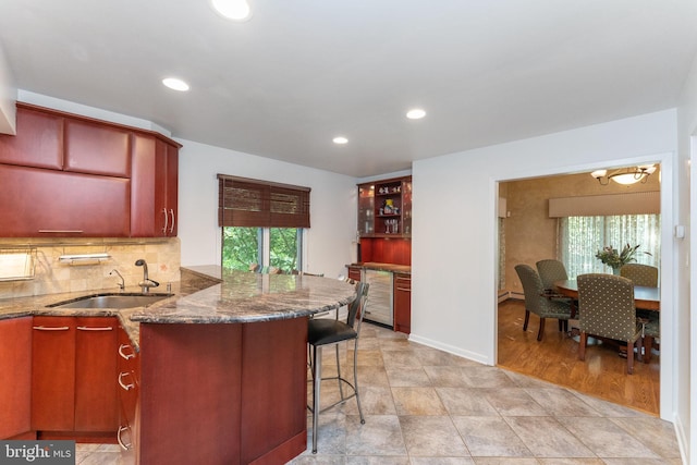 kitchen featuring backsplash, dark stone counters, a breakfast bar area, recessed lighting, and a sink