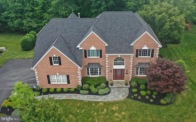 view of front facade with brick siding, a front yard, and a shingled roof