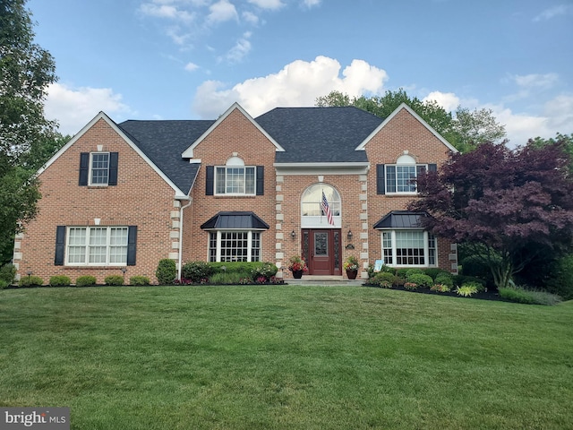 view of front of home with brick siding, a shingled roof, and a front lawn