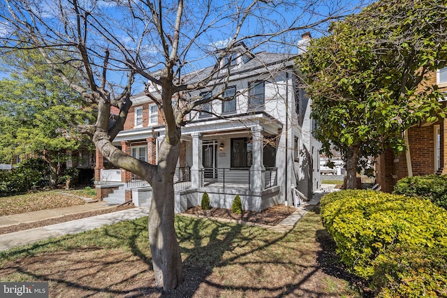 american foursquare style home featuring brick siding, covered porch, a chimney, and a front lawn